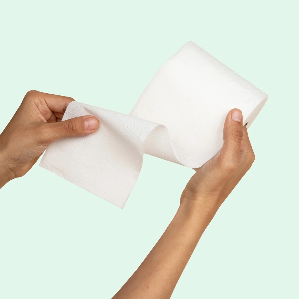Hands pulling a sheet from a roll of bamboo toilet paper